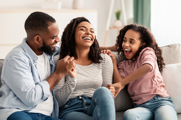 Portrait of a happy black family tickling sitting on couch - obrazy, fototapety, plakaty