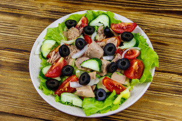 Tasty tuna salad with lettuce, black olives and fresh vegetables on wooden table