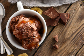Chocolate coconut vegan ice cream in a white cup. Ice cream balls with chocolate and caramel. Wooden background, copy space.