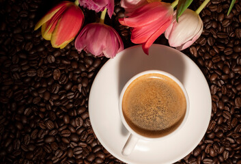 Cup of coffee and a bouquet of tulips on the background of roasted coffee beans