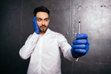 Shocked surprised doctor hold vaccine vial in laboratory. Liquid solution medication, drug. Vaccination concept. Man wear white shirt uniform, face mask blue gloves. Coronavirus healthcare
