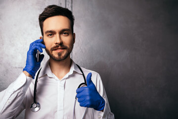 Man talking speaking hold phone modern gadget show thumb up like gesture. Doctor nurse dressed in white shirt with blue viral disposable face mask gloves stethoscope neck. Copy space 
