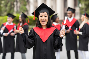 Delighted asian young lady student in graduation costume