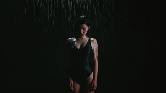 Portrait of Woman in a black swimsuit standing under the rain with sad face. Concept of loneliness, depression. Brunette is trying to cope with her resentment and fear. Girl stands completely alone