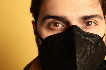 Close-up of man in black medical mask. Over yellow background.