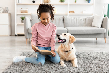 Young black girl reading book with dog at home