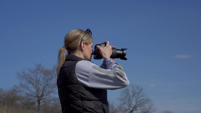 Woman photographer takes pictures outdoors against the blue sky. Blank space to insert your text.