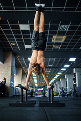 Athletic boy doing exercise on uneven bars in gym