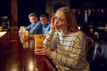 Bored girl drinks coctail at the counter in bar