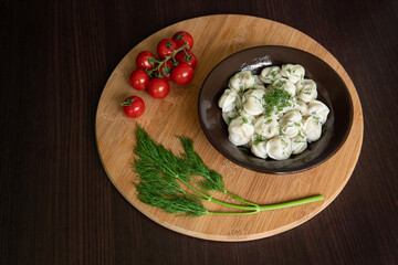 Fototapeta na wymiar Meat dumplings in brown dish on round wooden cutting board with cherry tomatoes and dill branch.