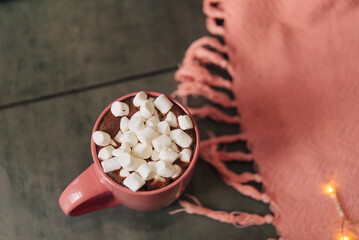 
hot chocolate or coffee and marshmallows in a pink glass. The cup stands on a grunge gray background near a pink plaid