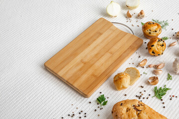 Fototapeta na wymiar Empty wooden cutting board with homemade bread, spices and greens on white textured vintage background, copy space.