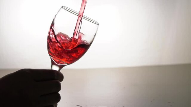 Close-up of pouring red wine into goblet in hand and shaking the glass, slow motion