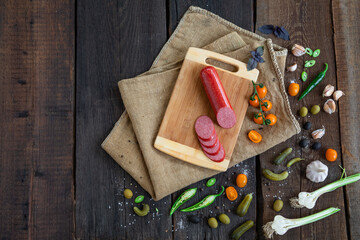 Fototapeta na wymiar Salami sausage on wooden cutting board with cherry tomatoes, chilli pepper, basilic, garlic, olives, cucumber and spices on vintage wooden background. Copy space.