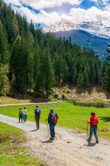 Hikers walking in mountains on a beautiful sunny day. Group of people hiking in mountains in spring when meadows are green and snow still on mountain peaks. Trentino-South Tyrol, Italy