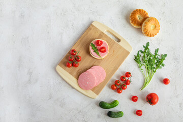 Breakfast with homemade sandwich with sausage slices on cutting board, tomatoes, cucumber, arugula and uzbek national bread on white vintage textured background. Copy space, top view.