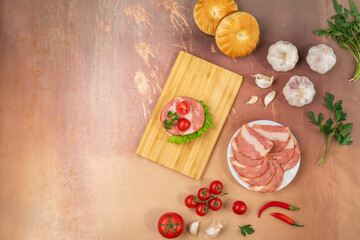 Sandwich with ham on wooden cutting board with greens, vegetables, tomatoes, bread and peppers on pink vintage background with copy space. Top view.