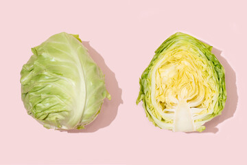 Whole head of fresh early cabbage and half of cabbage on a pink background.