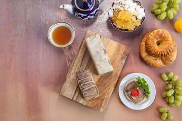 Uzbek breakfast pakhtagul teapot and cup with homemade sausage on cutting board and sandwich on white plate with bread, sugar and grapes on on pink background. Top view. Copy space.