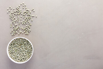 Legumes in bowl and scattered in the background, green peas in a plate on a gray background, top view, copy space