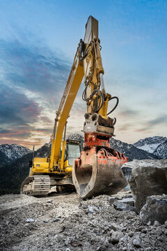 huge clamshell grab excavator for natural stone masonry in front of alp mountains and heavy rocks
