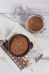 Organic uncooked scattered buckwheat grain in a bowl and glass jar on white wooden rustic background