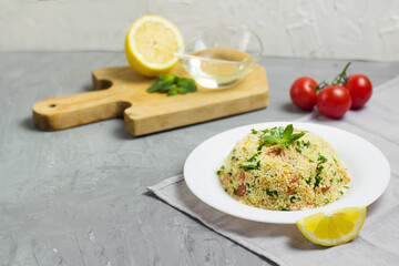 Traditional Arabic salad or Tabbouleh on white plate, healthy vegetarian dish with couscous on cement background