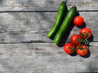 Cherry tomatoes on a green branch, two cucumbers on a gray wooden background. Fresh vegetables on the table. Horizontal photo.