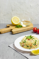 Traditional Arabic salad or Tabbouleh on white plate, healthy vegetarian dish with couscous on cement background