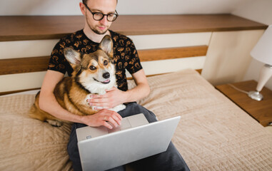 A young man working in a bedroom with a welsh corgi pembroke dog