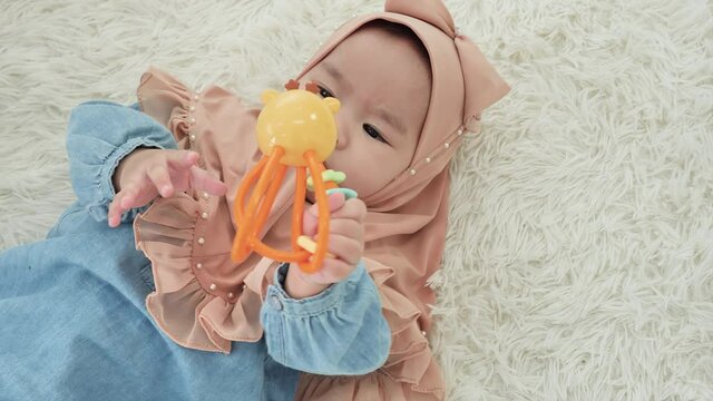 Top view Baby girl asian ethnicities 6 months old in traditional hijab clothing Lying Down playing toy on floor in bedroom. slow motion