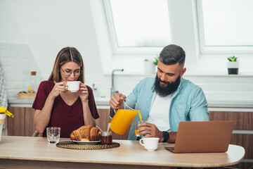Couple having breakfast at home while using a laptop