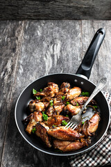 Roasted chicken wings in skillet on wooden table