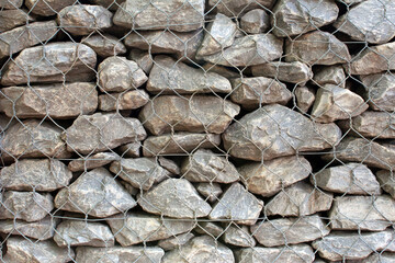 Background from a stone wall behind a metal grid. Stone background. Rockfall protection