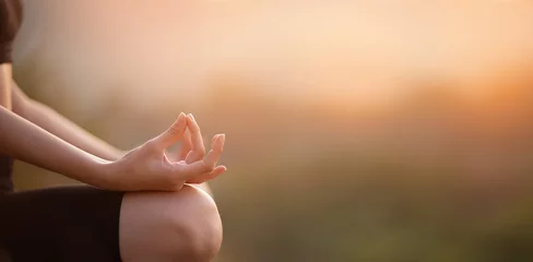 Fotobehang Close up with selective focus of hands woman sitting in yoga lotus pose outdoor at sunrise, meditating for balance. Horizontal banner view for website header design with copy space for text.  © Svetlana