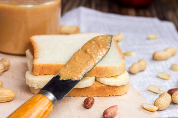 Homemade sandwich for breakfast with fresh crunchy peanut butter and bananas on light textile background.
