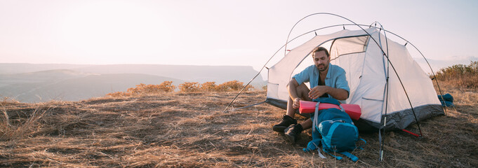 Young male tourist with a backpack in a tent in the mountains