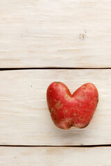 Heart shaped ugly potatoes on a beige background of wooden boards. Vegetable or food waste concept. Close-up.