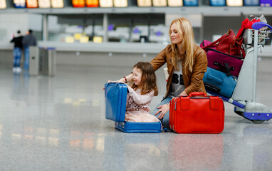 Cute little girl and mother at the airport. Tired family sitting on ground and waiting for delayed...