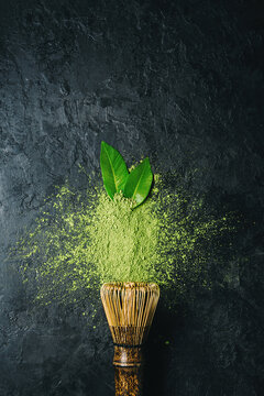 Matcha tea powder on dark background with whisk and leaves with copy space.