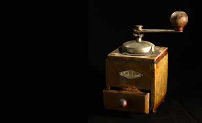 Antique coffee grinder with ground coffee on a black background