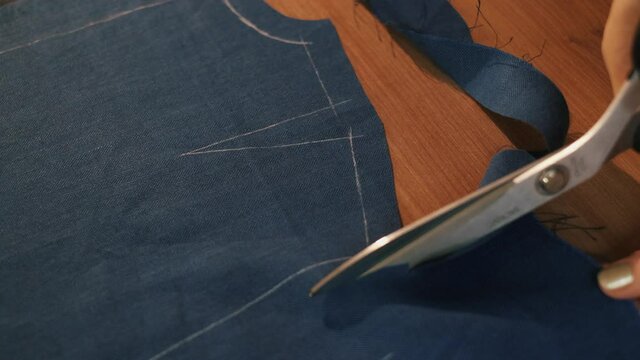 Hands cut the fabric with tailor's scissors, cutting a piece of fabric the concept of a fashion designer. Blue fabric for sewing clothes.