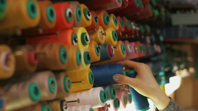 Spools of colored thread on a vertical stand. Close-up hand removes spools of thread