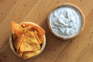 Nachos and yoghurt sauce with spice in wooden bowl. Spicy potato chips on wooden table. Snack food concept.