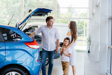 A happy young family chooses and buys a new car at a car dealership. Buying a new car