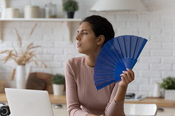 Too hot indoors. Exhausted young woman tired of online work at home office suffer breath warm dry...