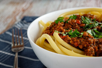 Close up of Italian pasta with bolognese, in a bowl. In the background a blue kitchen towel.