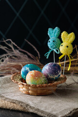 multi-colored Easter eggs of blue tones and two Easter bunny on a stick on a brown cloth background