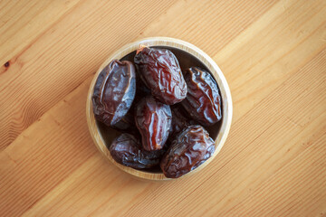 Top view of palm dates in wooden bowl on wooden table. Traditional muslim fruit. Ramadan culture concept.