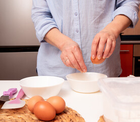 Obraz na płótnie Canvas The hands of an aged woman breaks an egg into a white bowl. Selective focus.
